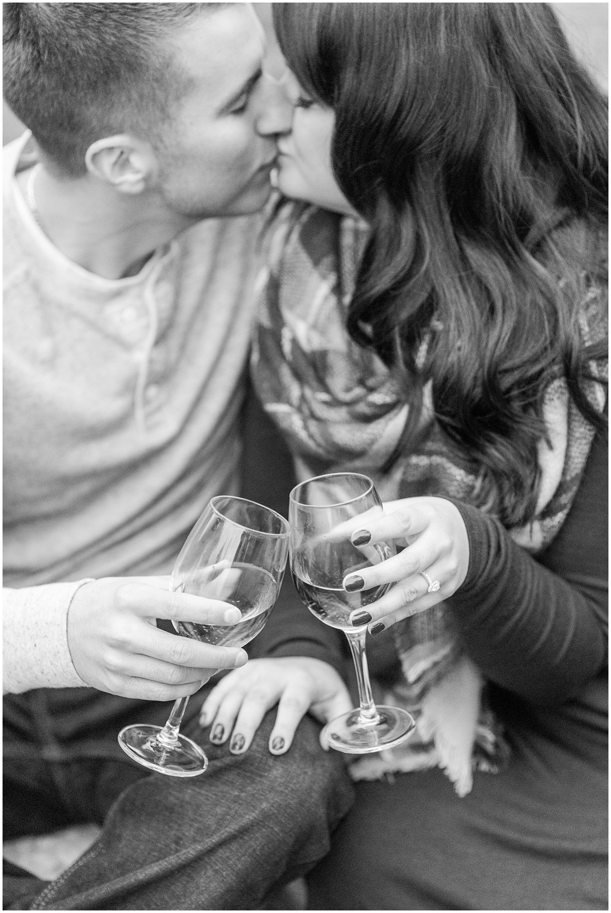 Bride to be kissing her fiance while holding wine glasses