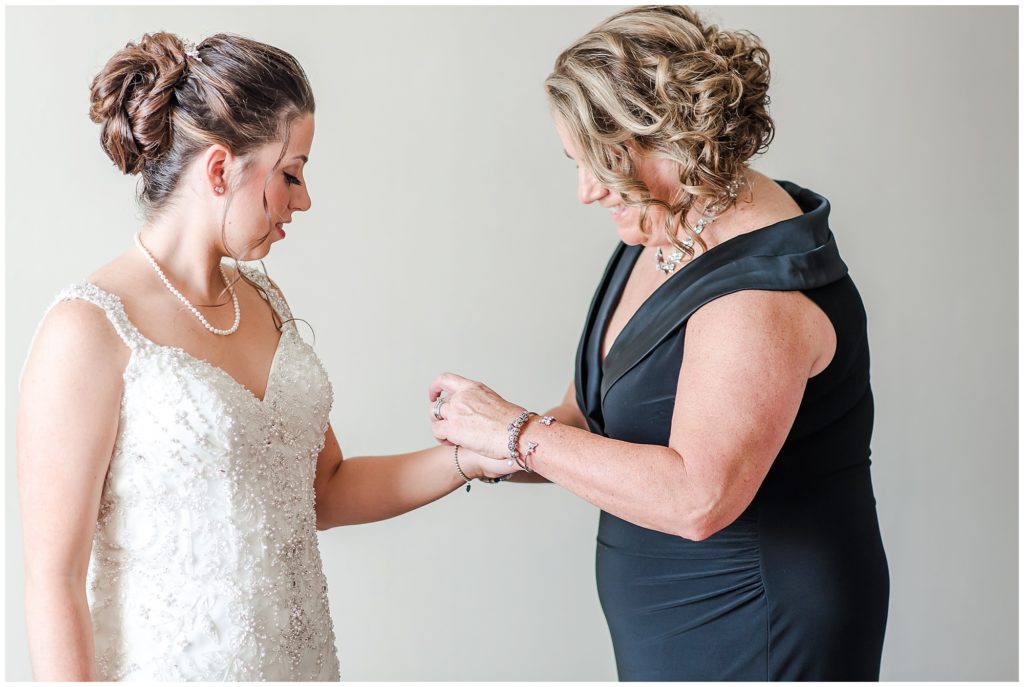 mother of the bride is helping to put a bracelet on the bride