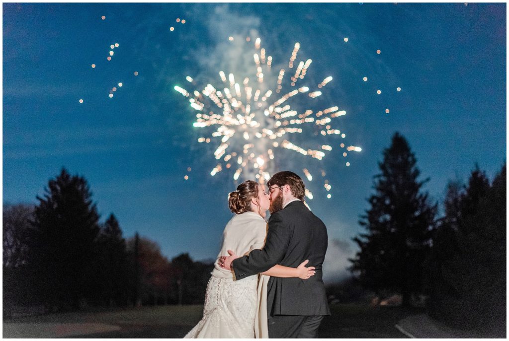 Bride and groom kissing with fireworks in the background