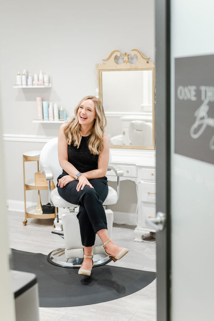 woman in black outfit smiling while sitting in a salon chair