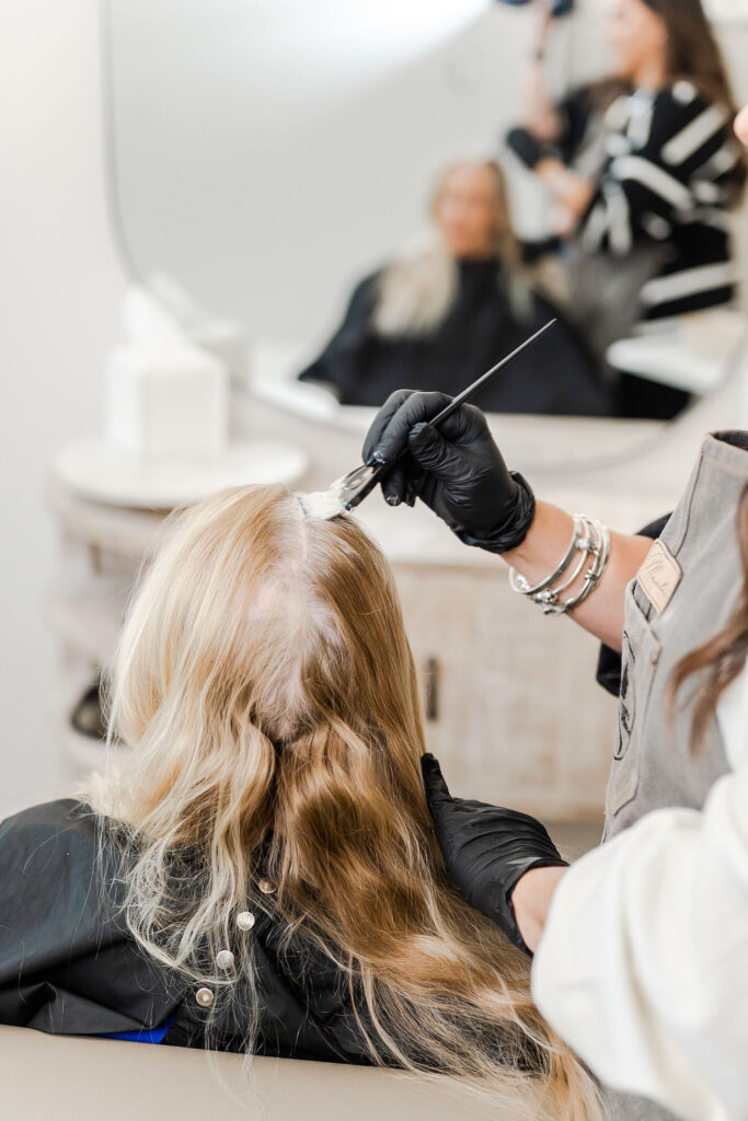 woman in black glove applying hair dye to a client's hair