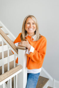 woman in orange smiling while standing at the bottom of a stairwell