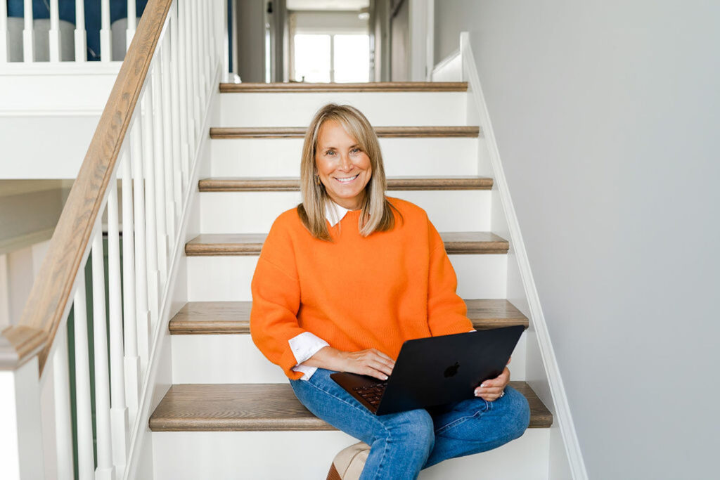 realtor holding a laptop and smiling while sitting on the stairs