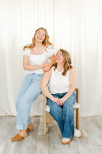women in white tank tops and jeans sitting next to each other and smiling during a salon branding session