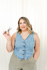 woman in denim vest smiling while holding scissors