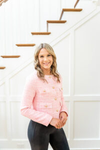 real estate agent in pink shirt and black pants smiling by a stairwell