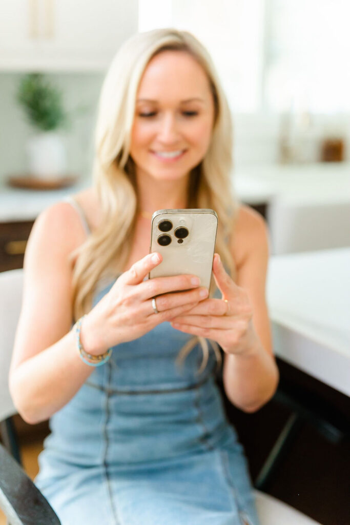 close-up photo of woman in denim dress smiling at her phone