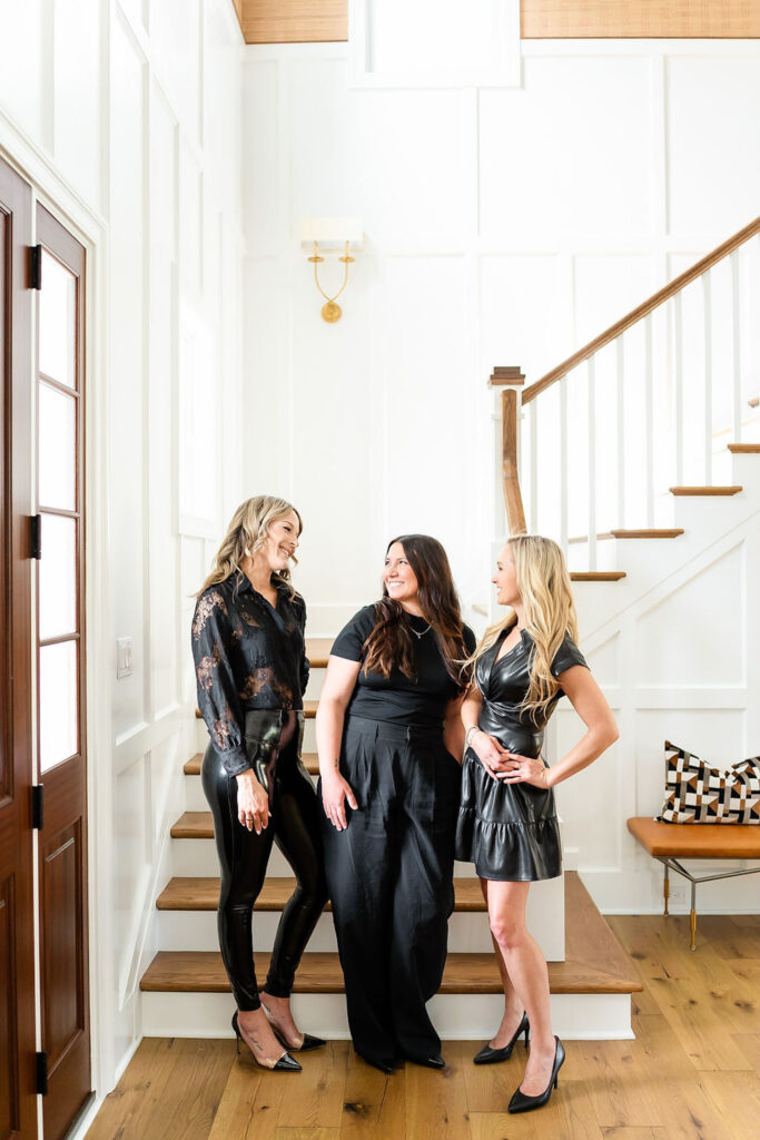 Team of real estate agents standing together by stairs, dressed in black outfits and smiling at each other — showcasing a united team presence.