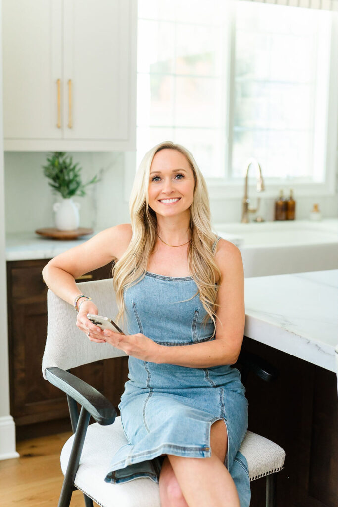 headshot of luxe local real estate agent, wearing a denim dress and sitting at the kitchen island