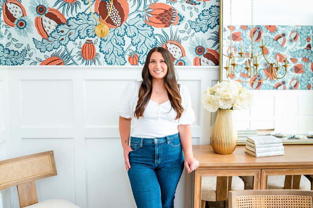 woman in white shirt and jeans smiling while standing in front of colorful wallpaper