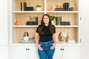 luxe local real estate agent standing in front of decor shelves while smiling