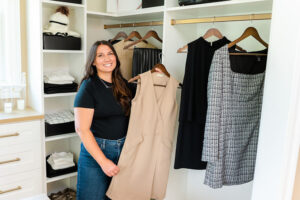 real estate agent standing by a closet while holding clothes, smiling at the camera