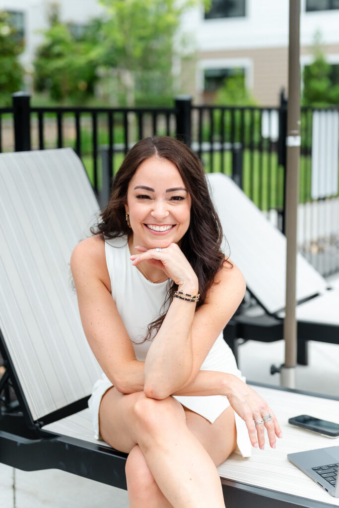 woman in white dress smiling while sitting on a pool lounger