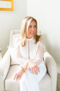 woman in white smiling into the distance while sitting on a sofa chair