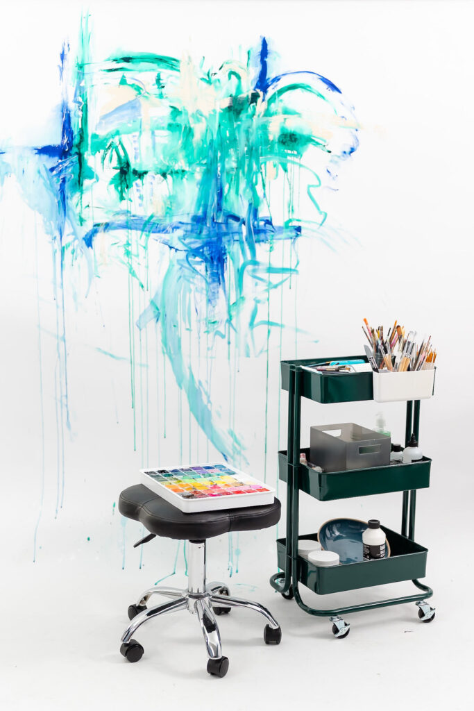 stool and cart full of art supplies with a painted wall behind it