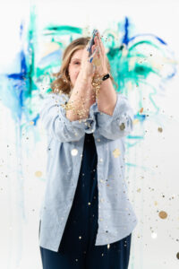woman standing in front of a painted wall while blowing confetti out of her hands during a branding session