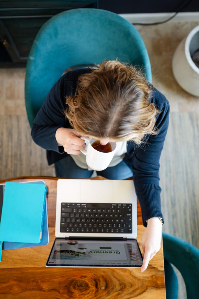 overhead view of an online coach working at her laptop while sipping coffee during a branding session