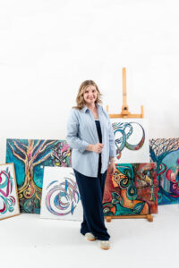 woman holding a canvas with artwork on it and multiple other pieces of art in the background