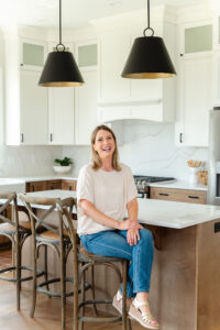 woman in jeans and a cream top sitting at the kitchen island and smiling