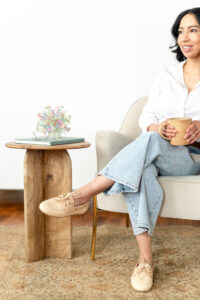 art therapist in blouse and jeans sitting in a chair and smiling into the distance