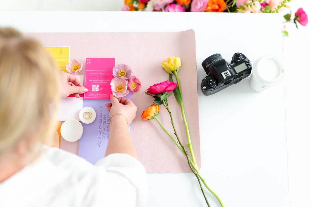 Brand Photo of a Wedding Photographer styling color wedding invitations on a styling mat with her DSLR camera and flowers